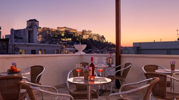 Una terrazza con sedie e tavoli in vimini, una bottiglia di vino e dei bicchieri, con vista su un edificio storico su una collina.