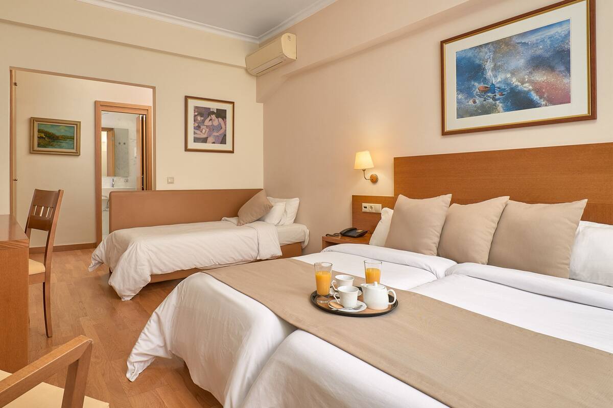 Habitación de hotel con dos camas, una bandeja de desayuno con jugo y café, un cuadro y un espejo.