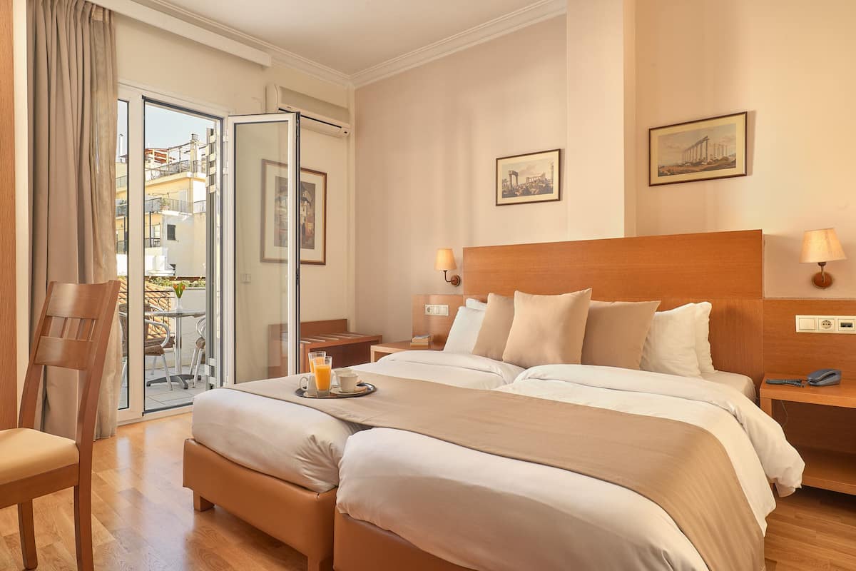 Habitación de hotel con una cama grande, una silla, una mesita de noche con lámpara y vistas al balcón exterior.