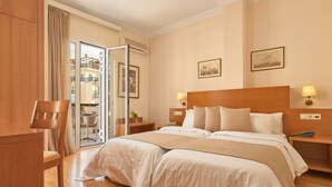 Camera d'albergo con due letti, una sedia di legno, una scrivania e vista sul balcone esterno.