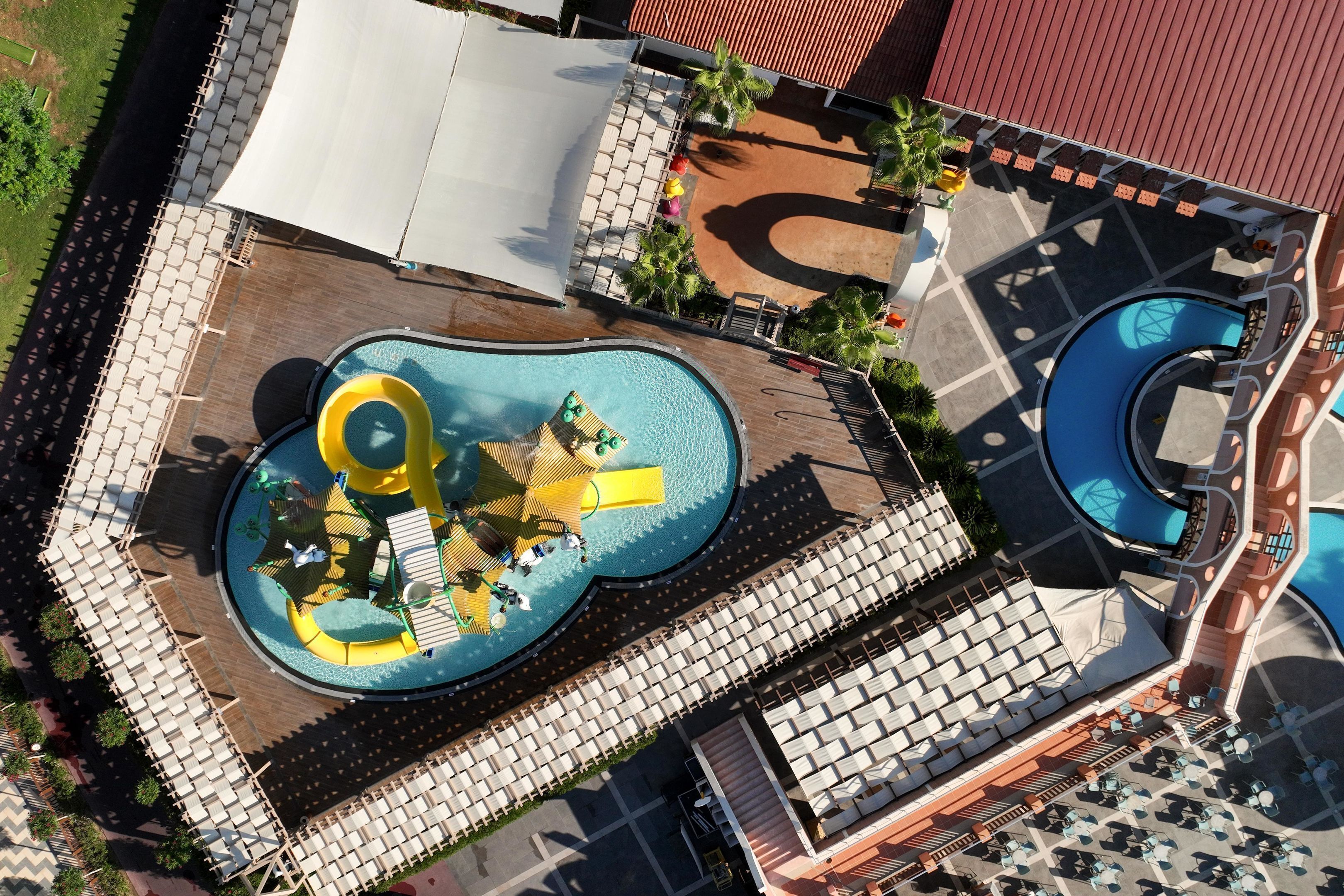 An aerial view of a resort with a large pool area, sun loungers, and a water slide.