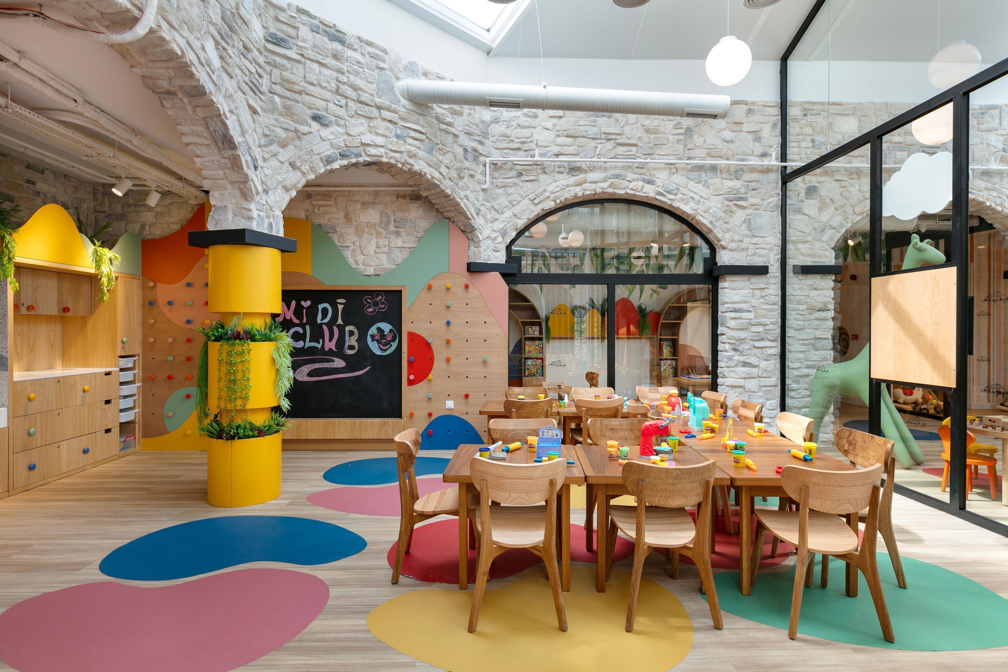Zona de jocs infantil amb mobles de fusta, estores de joc de colors i una paret de pissarra.