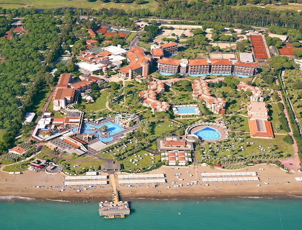 An aerial view of a resort with multiple buildings, a large swimming pool, and a beach area. - Megasaray Club Belek (Serik)