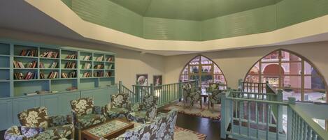 A library with bookshelves, floral-patterned chairs, a table, and a staircase with a view outside.