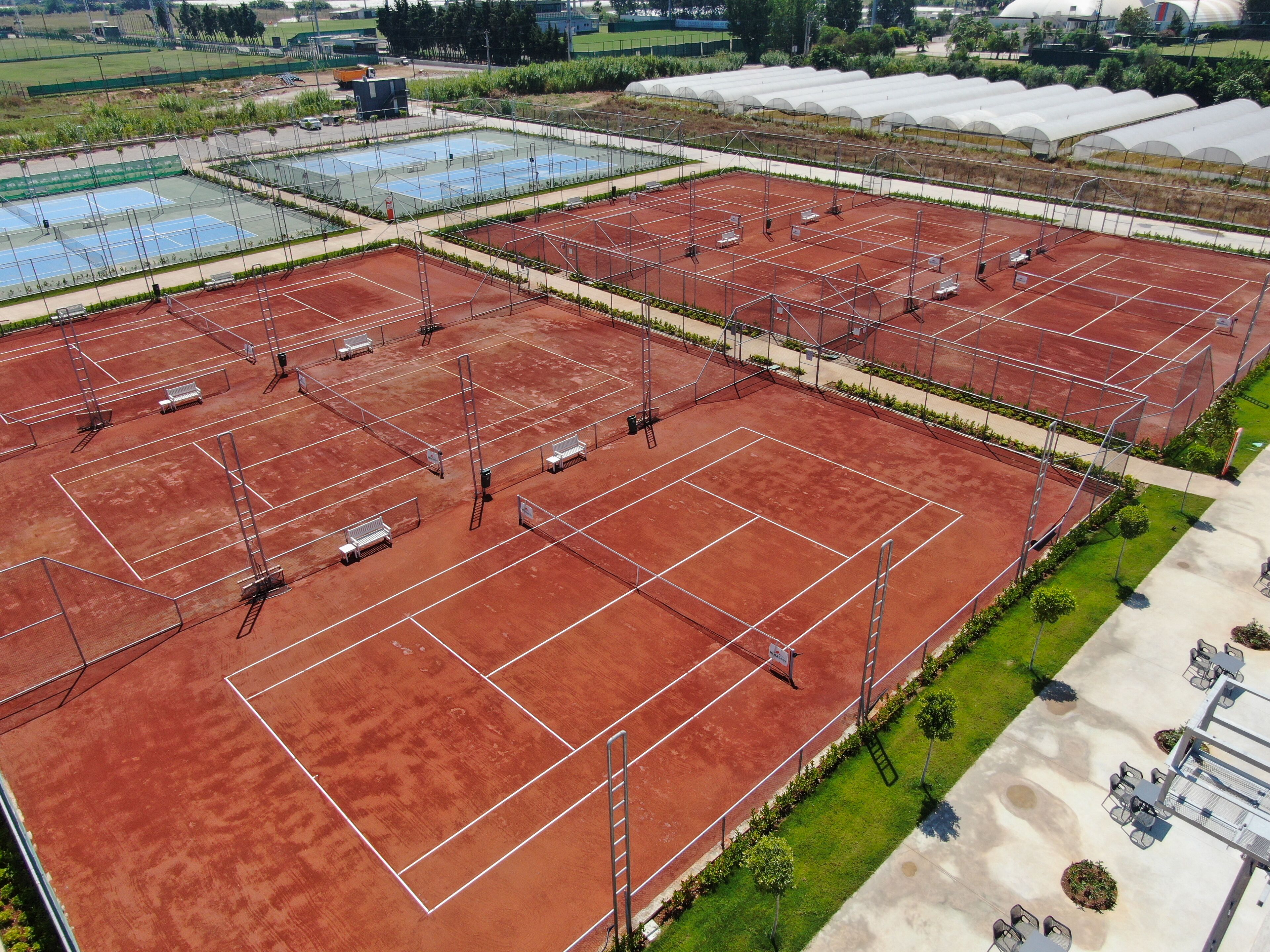 Ein großer Sportkomplex mit mehreren Tennisplätzen, Grünflächen und einem überdachten Bereich mit Pflanzen.