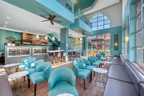 A spacious lounge area with teal-colored seating, a bar with a menu, and a staircase leading to an upper level.