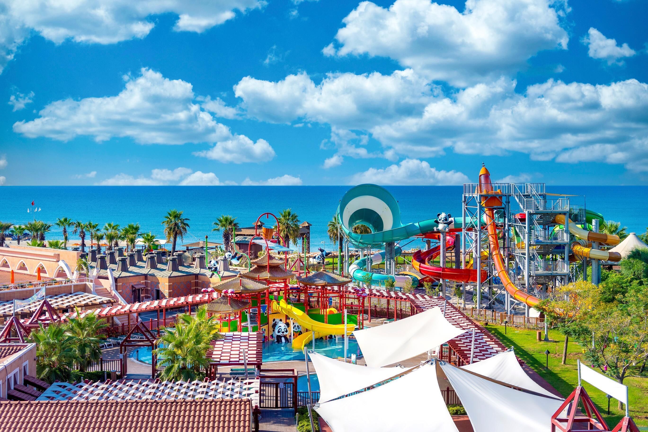 A water park with slides and pools, surrounded by palm trees and a view of the ocean.