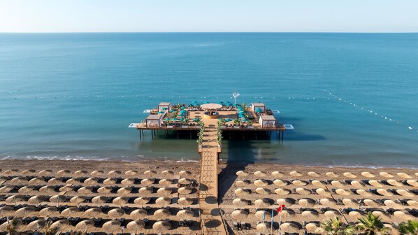 Überwasserbungalows mit einer Holzterrasse und Liegestühlen, verbunden mit dem Strand durch einen Holzsteg.