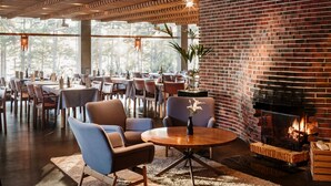 A restaurant with a brick fireplace, round tables, and blue chairs. - Hotel Rantapuisto (Helsinki)