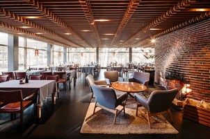 Un ristorante moderno con parete in mattoni, soffitto in legno e ampie finestre. Tavoli e sedie disposti per la ristorazione.