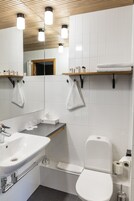 Un bagno moderno con lavandino, vaso e specchio bianchi. Asciugamani appesi a ganci e uno scaffale con articoli da toilette.