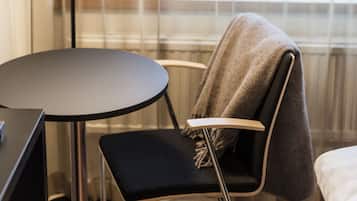 Una habitación con una cama, una mesita redonda pequeña, una silla, una lámpara de pie y un ventanal con cortinas.