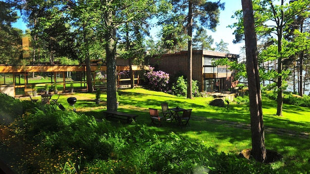 A modern building with a glass facade, surrounded by lush greenery and trees. - Hotel Rantapuisto (Helsinki)