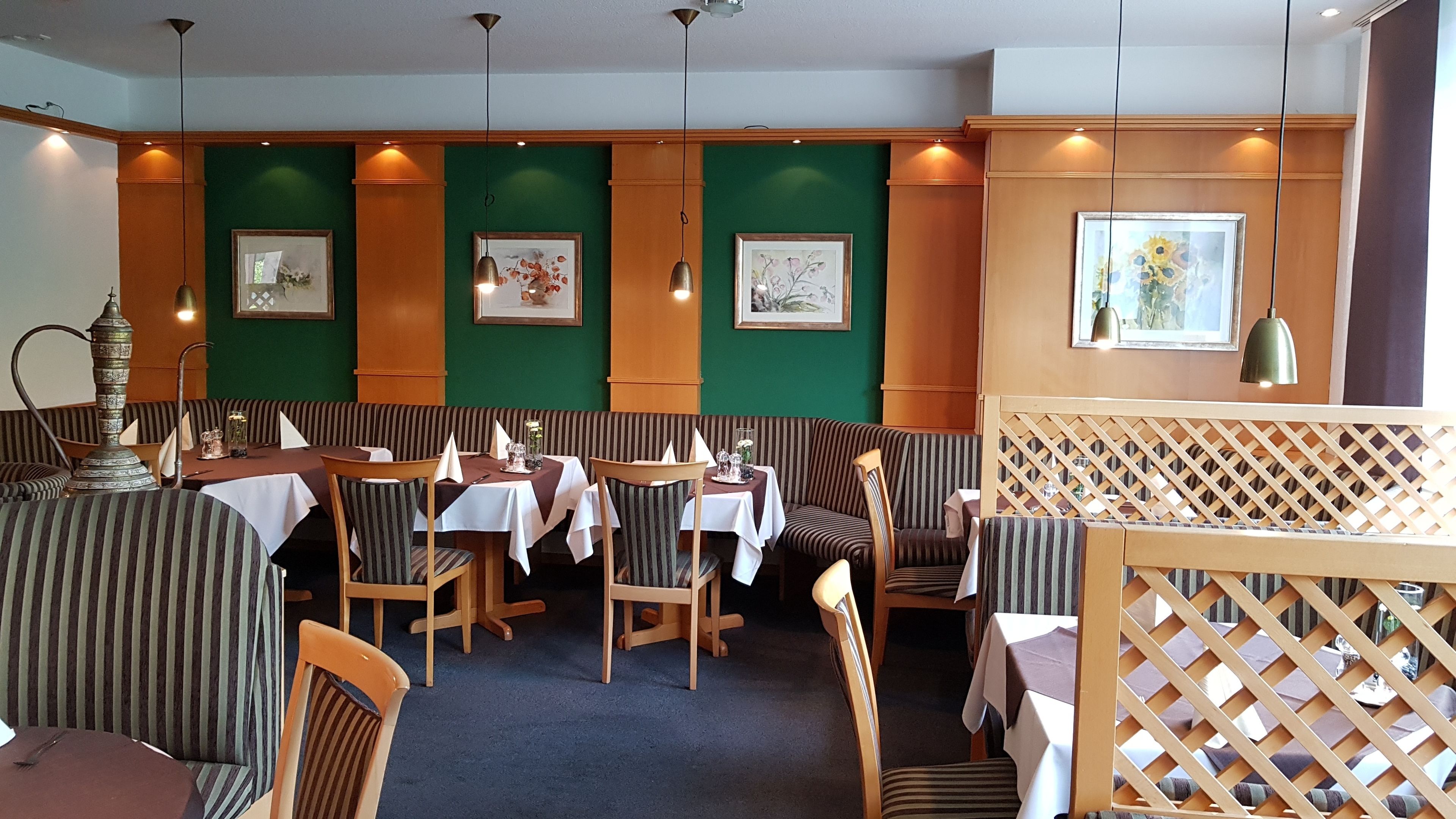 En restaurang med randiga bås och bord, gröna väggar och inramade konstverk.
