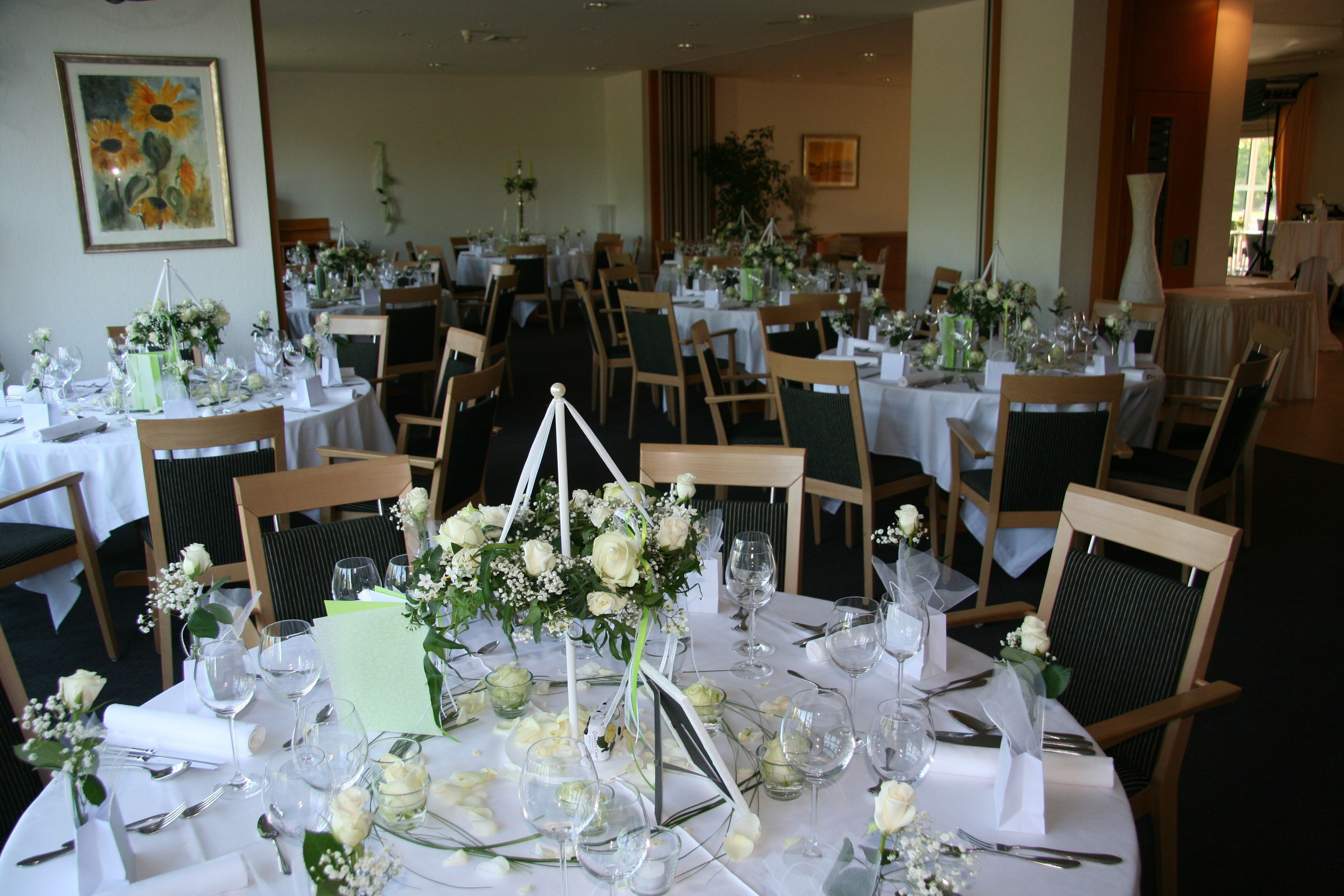 A dining area with round tables set for a formal event, featuring floral centerpieces and white tablecloths.