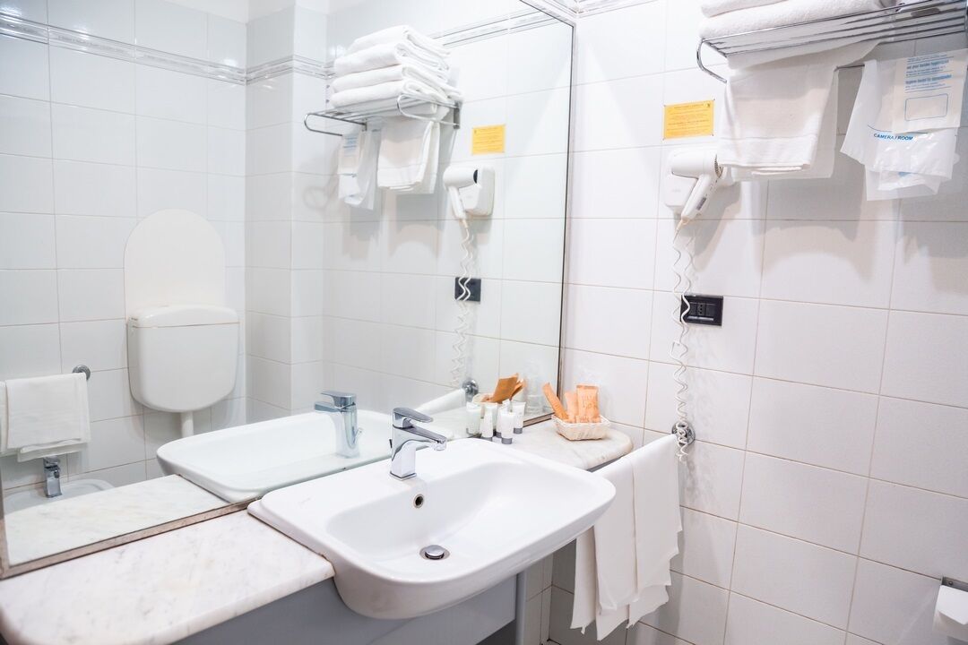 Bagno d'albergo con due lavandini, un water, uno specchio e porta asciugamani.