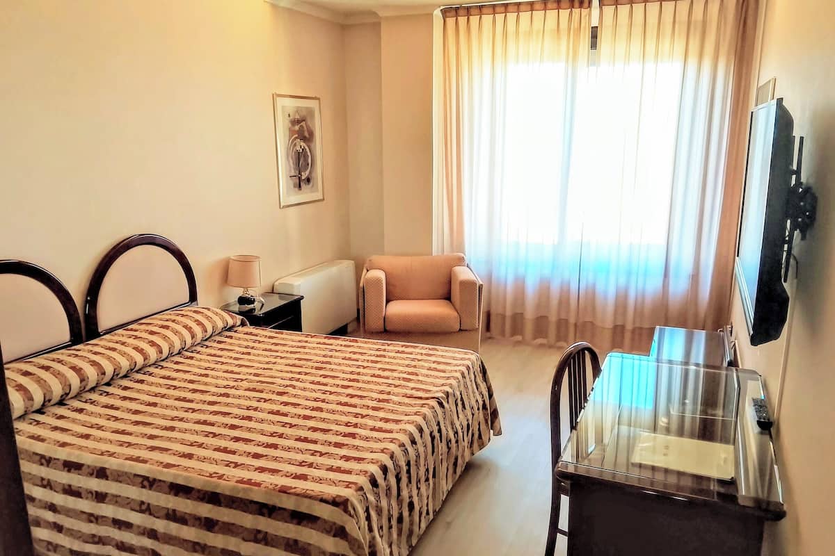 Een hotelkamer met een bed, een stoel, een bureau met spiegel, een televisie en een raam met gordijnen.