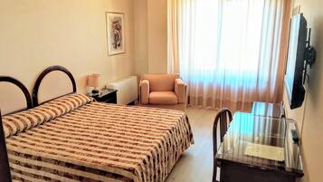 A hotel room with a bed, a chair, a desk with a mirror, a television, and a window with curtains.