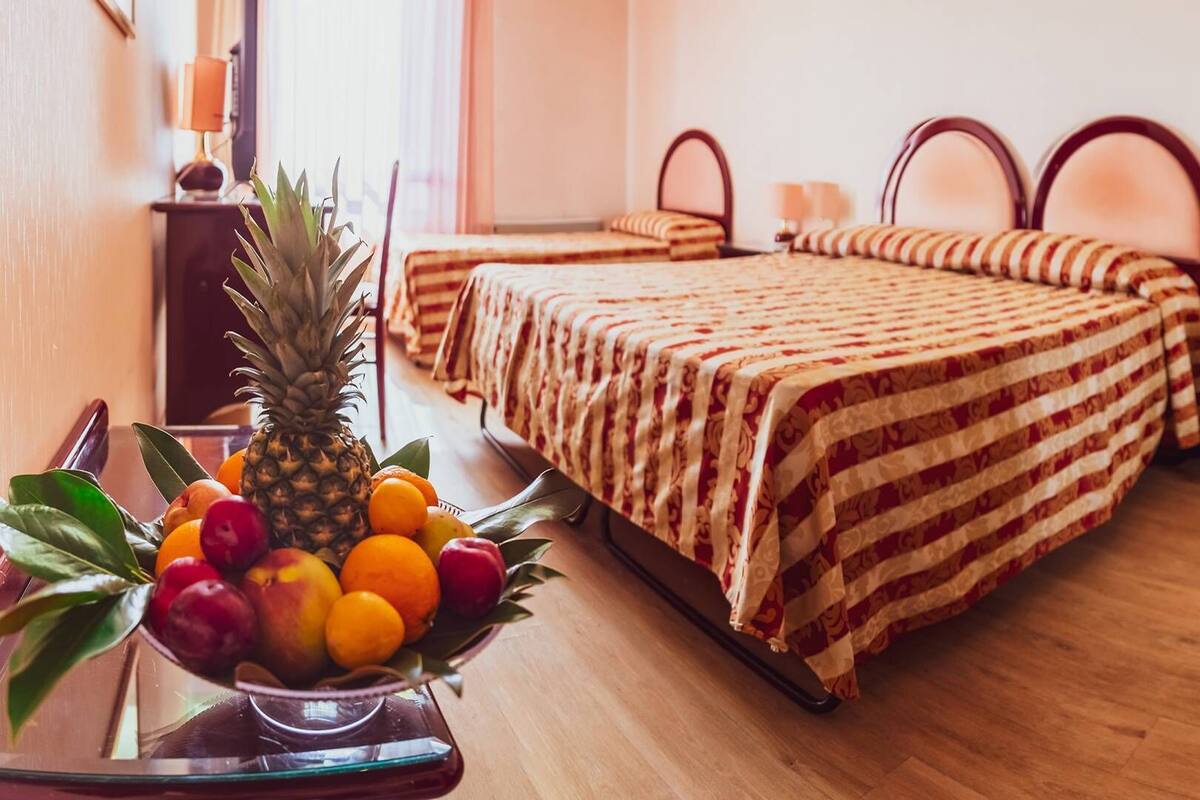 Een hotelkamer met twee bedden, een fruitschaal op een tafel en een lamp op een nachtkastje.