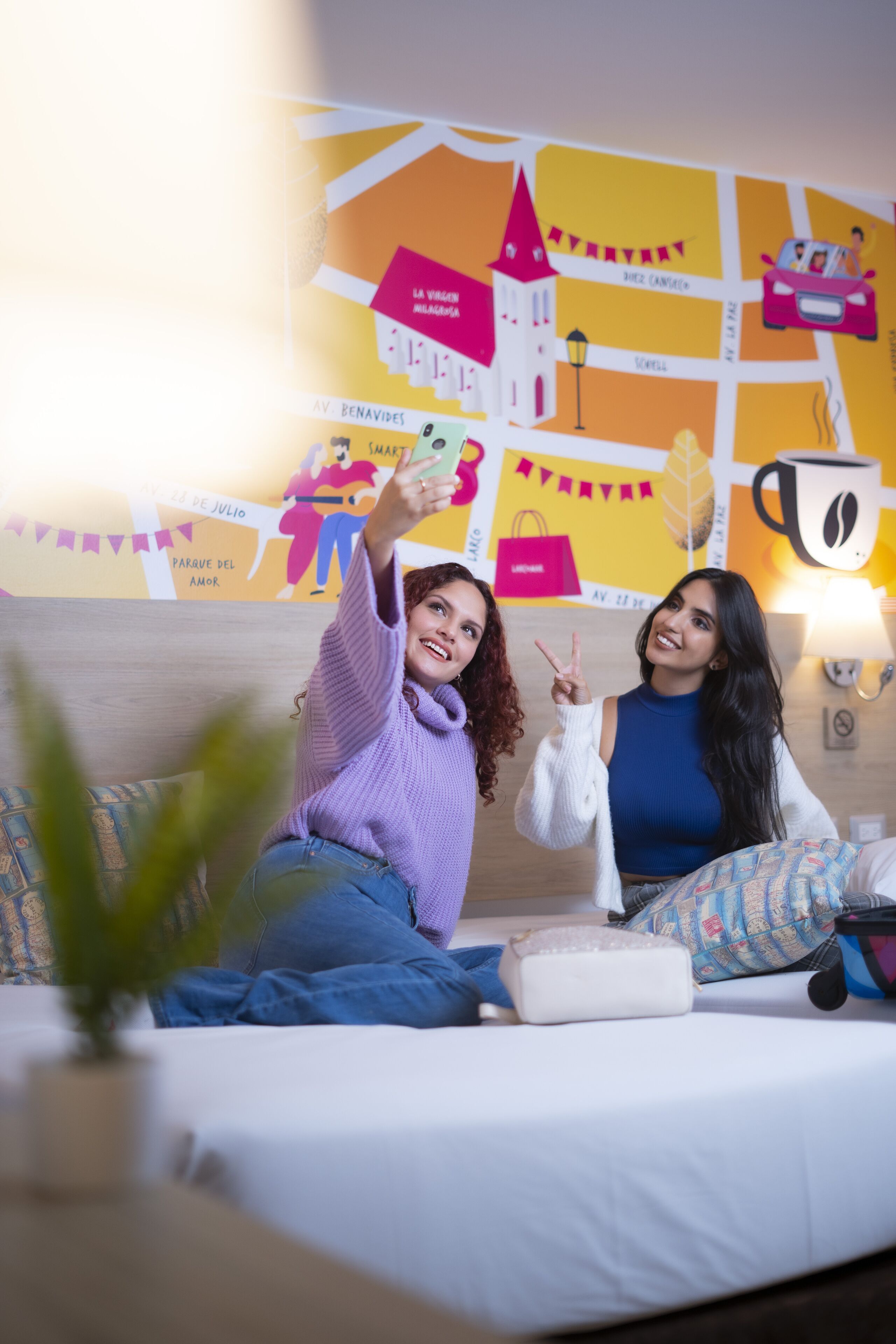 A room with a bed, pillows, a plant, and a wall with colorful decorations.