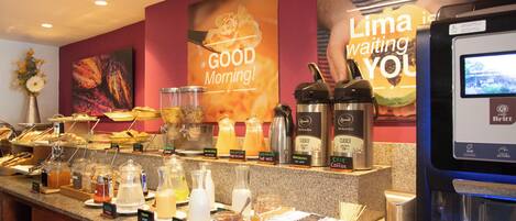 Zona de desayuno tipo bufé con diversas opciones de comida y una máquina de café.