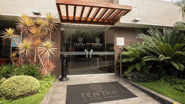 A building entrance with a glass door, a wooden pergola, and a doormat with the building's name.
