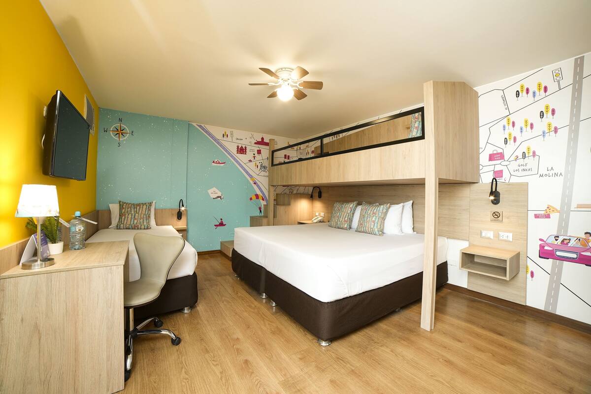 Ein kompaktes Hotelzimmer mit Etagenbett, Schreibtisch mit Stuhl, Schreibtischlampe, kleiner Pflanze und einer Wandkarte.