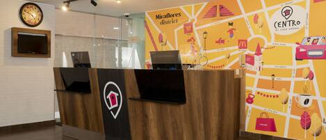 A reception desk with a wooden finish, a clock, and a map of the Miraflores district on the wall.
