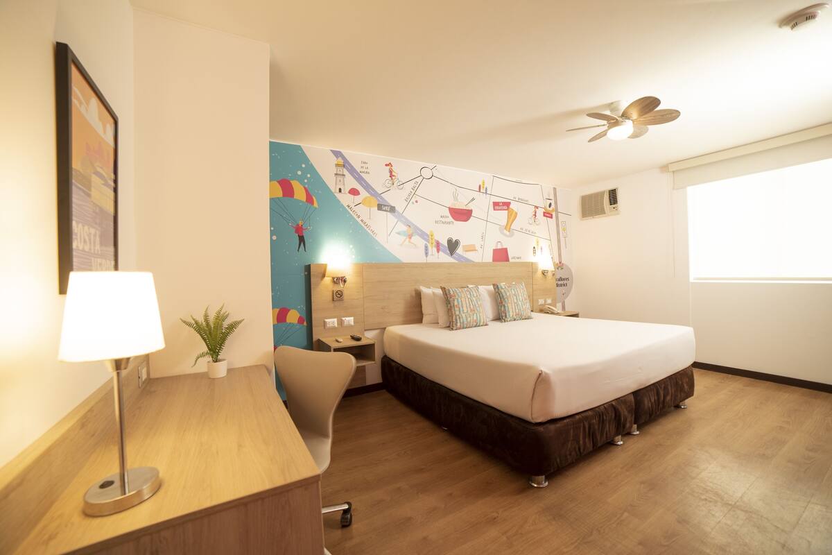 Ein Hotelzimmer mit Bett, Nachttisch, Lampe und einer Wandkarte.