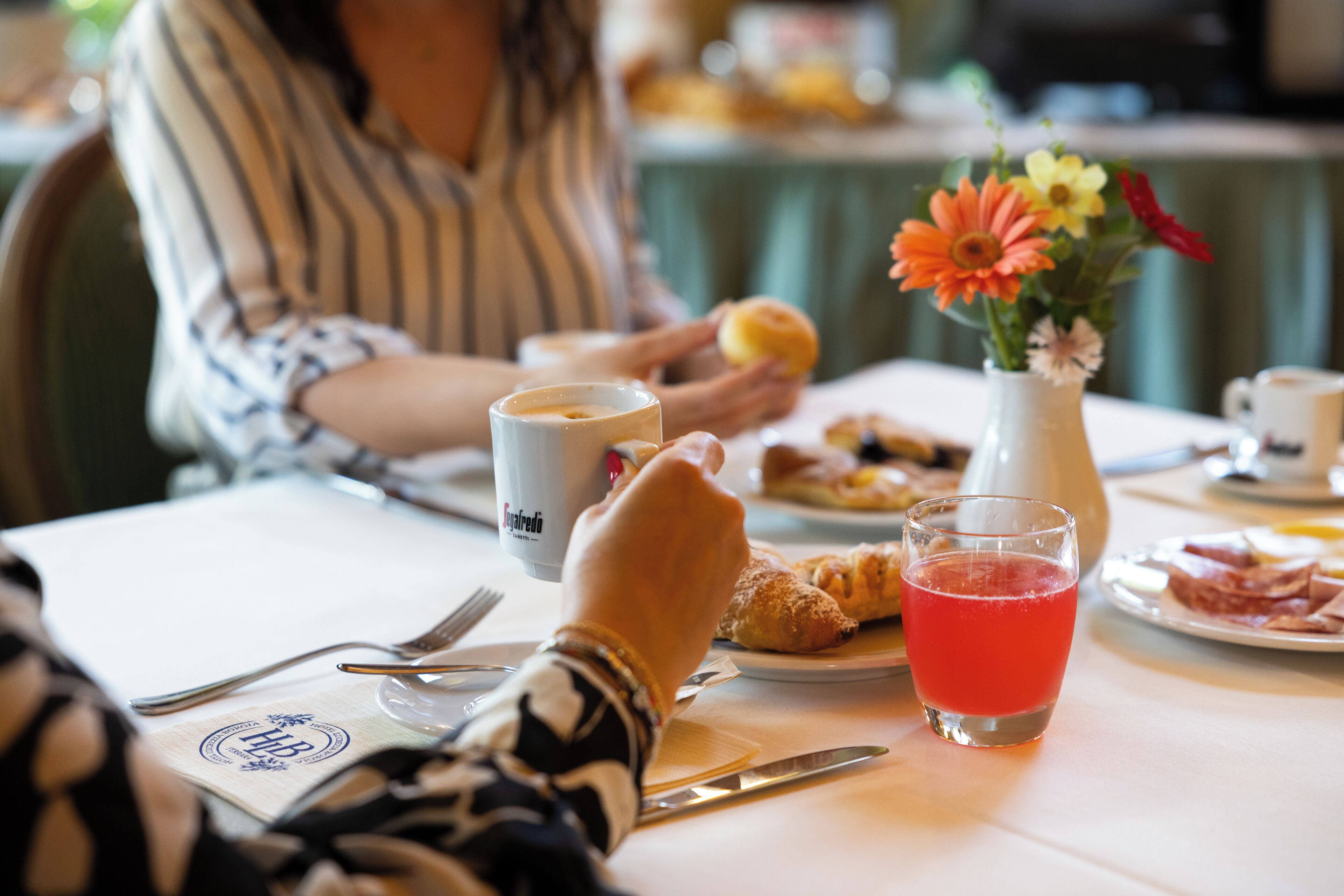 Ein Esstisch mit einem Teller Essen, einem Glas roter Flüssigkeit und einer Vase mit Blumen.