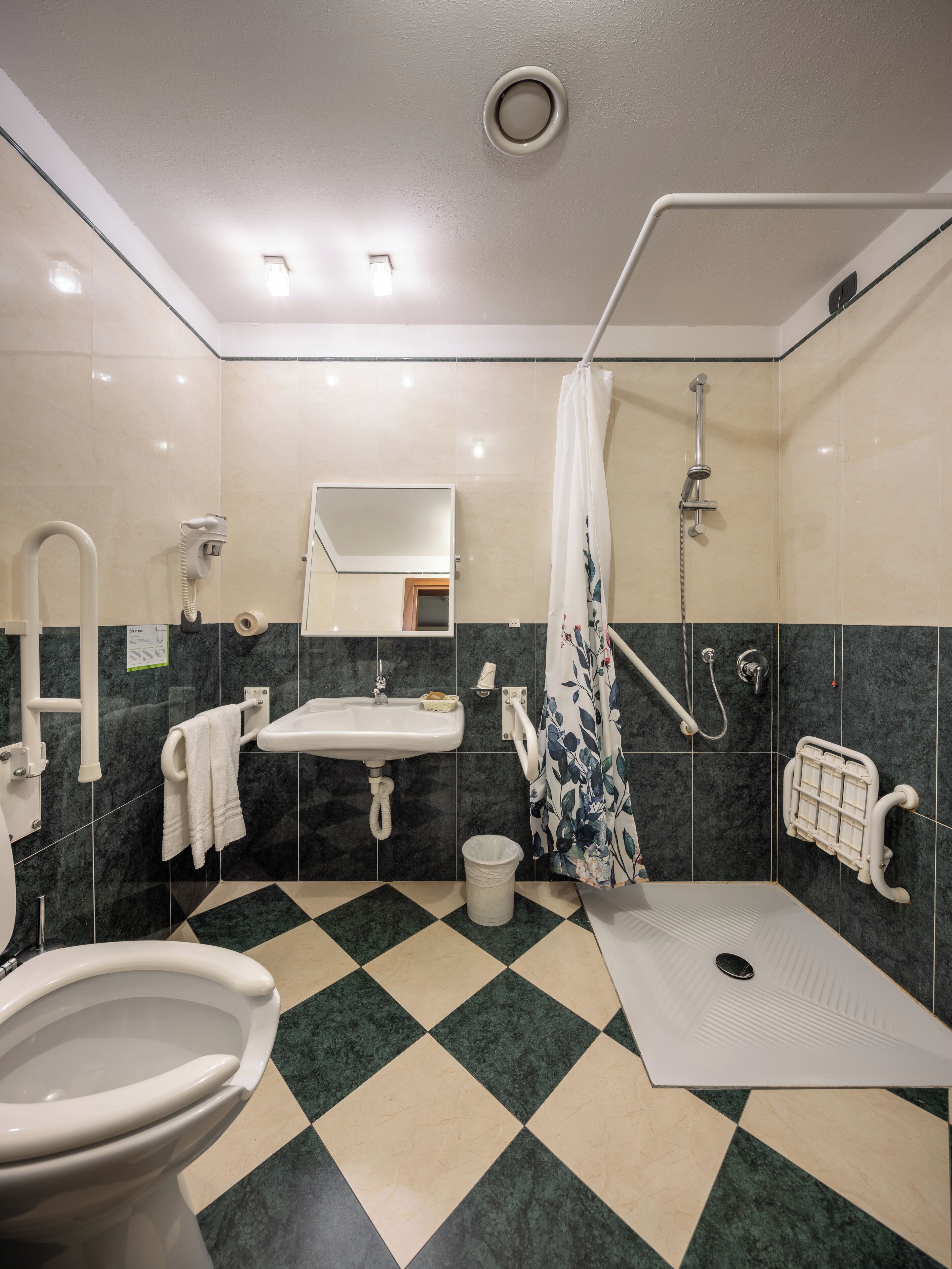 A modern bathroom with a toilet, sink, shower, and grab bars.