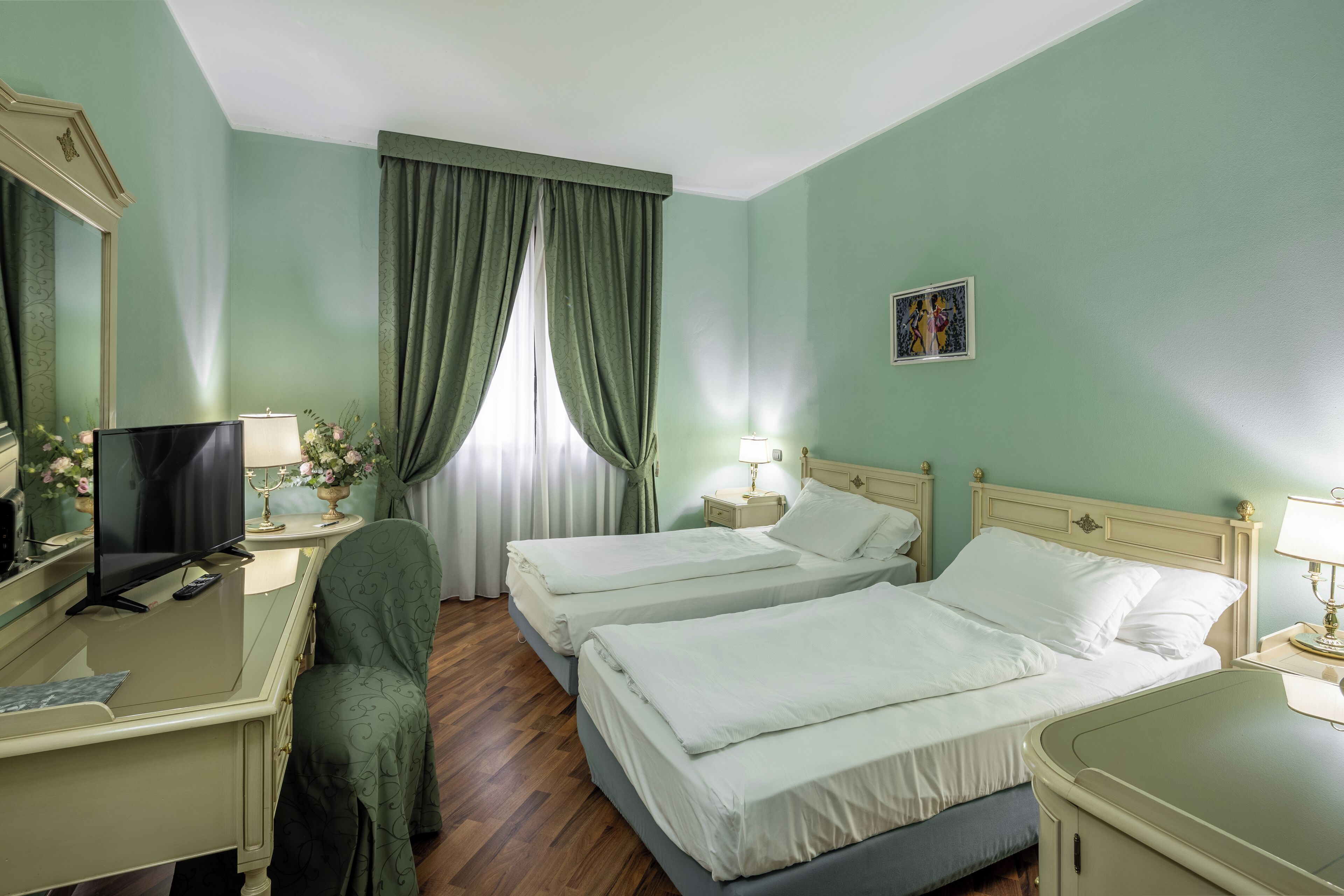 A hotel room with two beds, a desk with a television, and a mirror.
