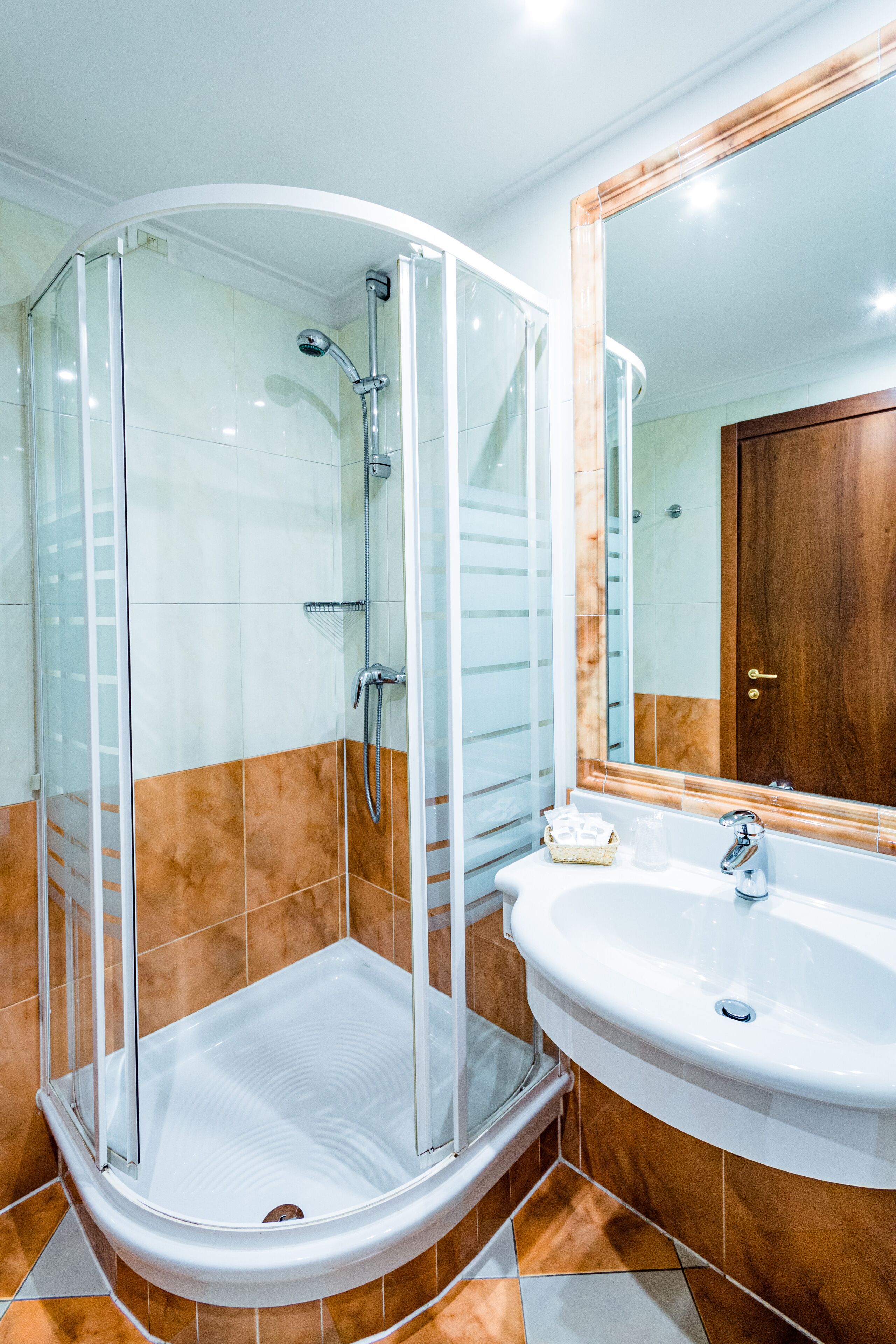 Un baño con ducha de vidrio, lavamanos blanco y puerta de madera.