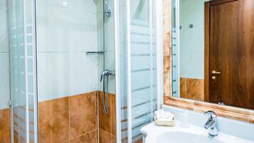 Un baño con ducha de vidrio, lavamanos blanco y puerta de madera.