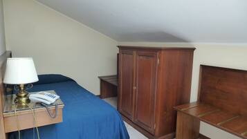 A bedroom with a bed, a wooden wardrobe, a bedside table with a lamp, and a telephone.