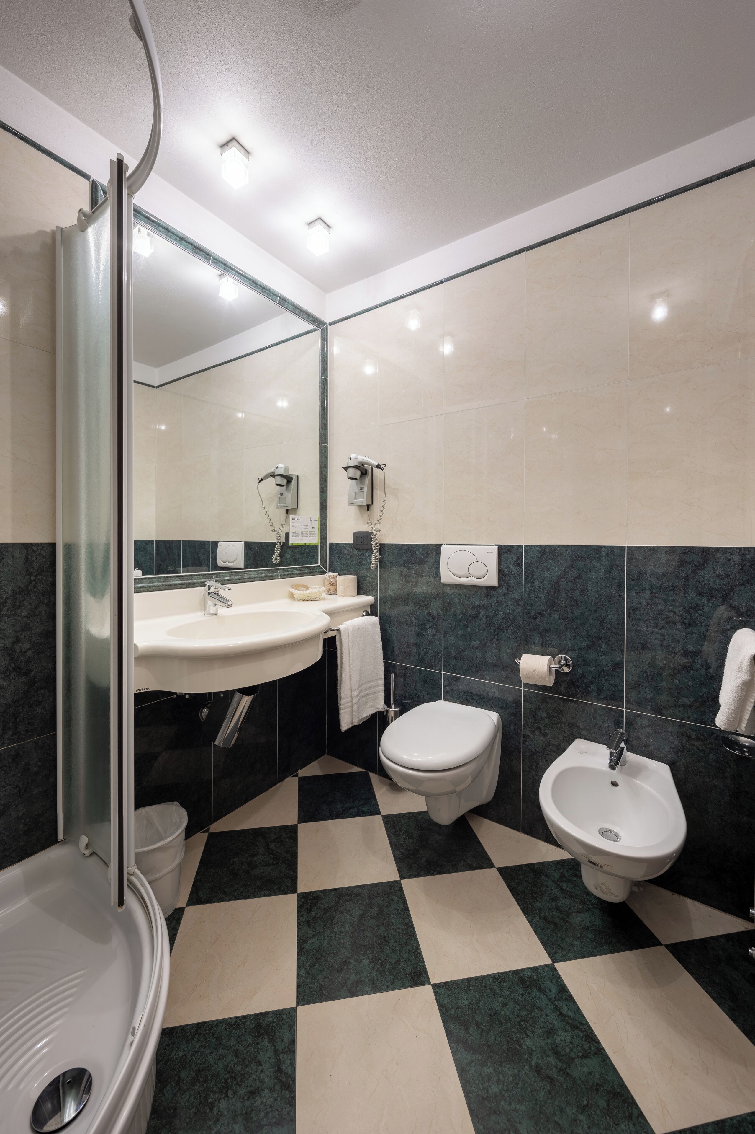 Un bagno moderno con pavimento a scacchi, cabina doccia in vetro, lavabo, water e bidet.