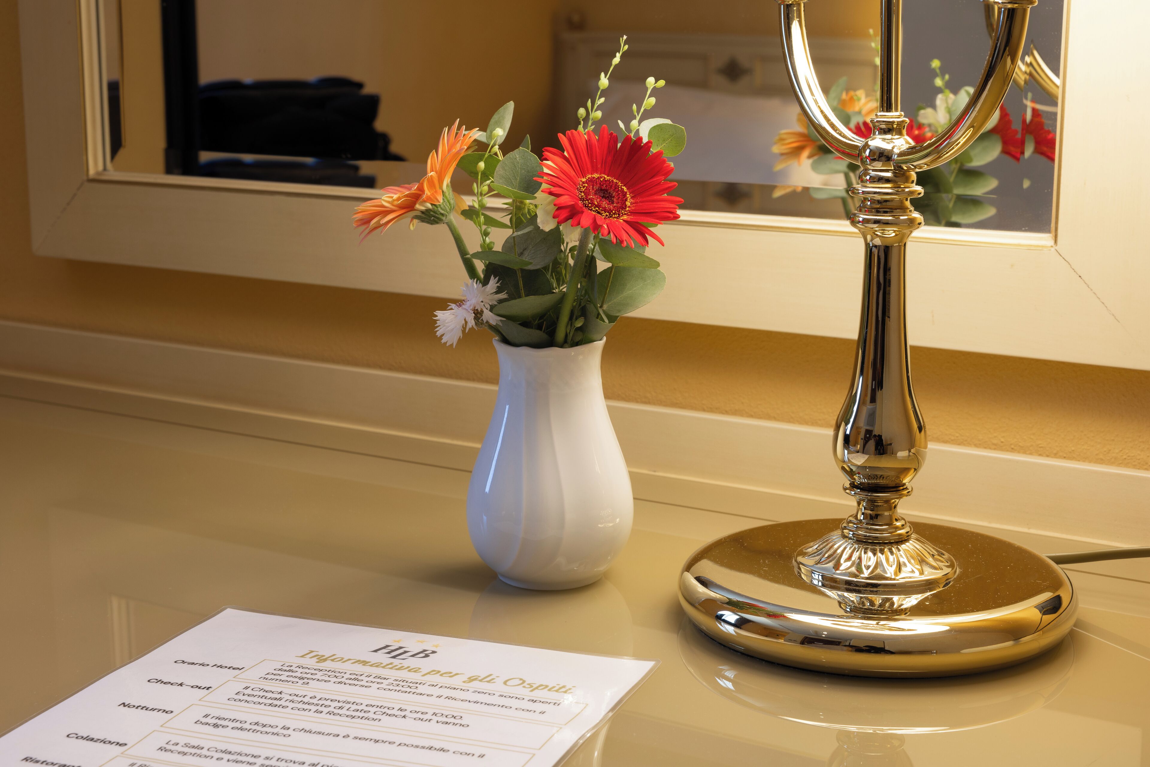 Eine weiße Vase mit Blumen auf einem Tisch, ein Spiegel, der einen Raum reflektiert, und eine Speisekarte auf dem Tisch.