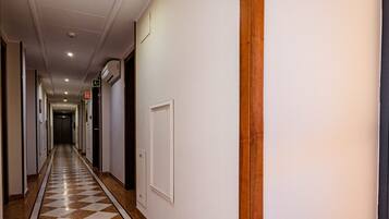 A hotel hallway with a checkered floor, doors on both sides, and signs indicating directions.