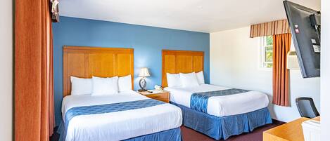 A hotel room with two beds, a desk, and a television.