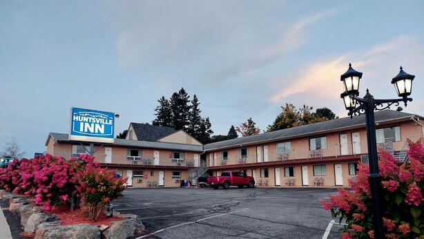 A Huntsville Inn motel with a two-story structure, a parking lot, and a red vehicle parked in front. - Huntsville Inn (Huntsville)