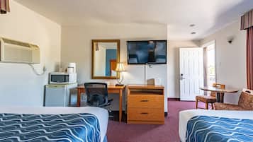 A hotel room with two beds, a desk with a chair, a television, a microwave, and a small table with a chair.