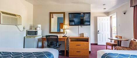Habitación de hotel con dos camas, un escritorio con silla, televisor, microondas y una pequeña mesa con una silla.