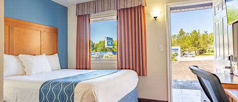 Une chambre d’hôtel avec un lit, un bureau, une fenêtre avec des rideaux et une vue sur l’extérieur.