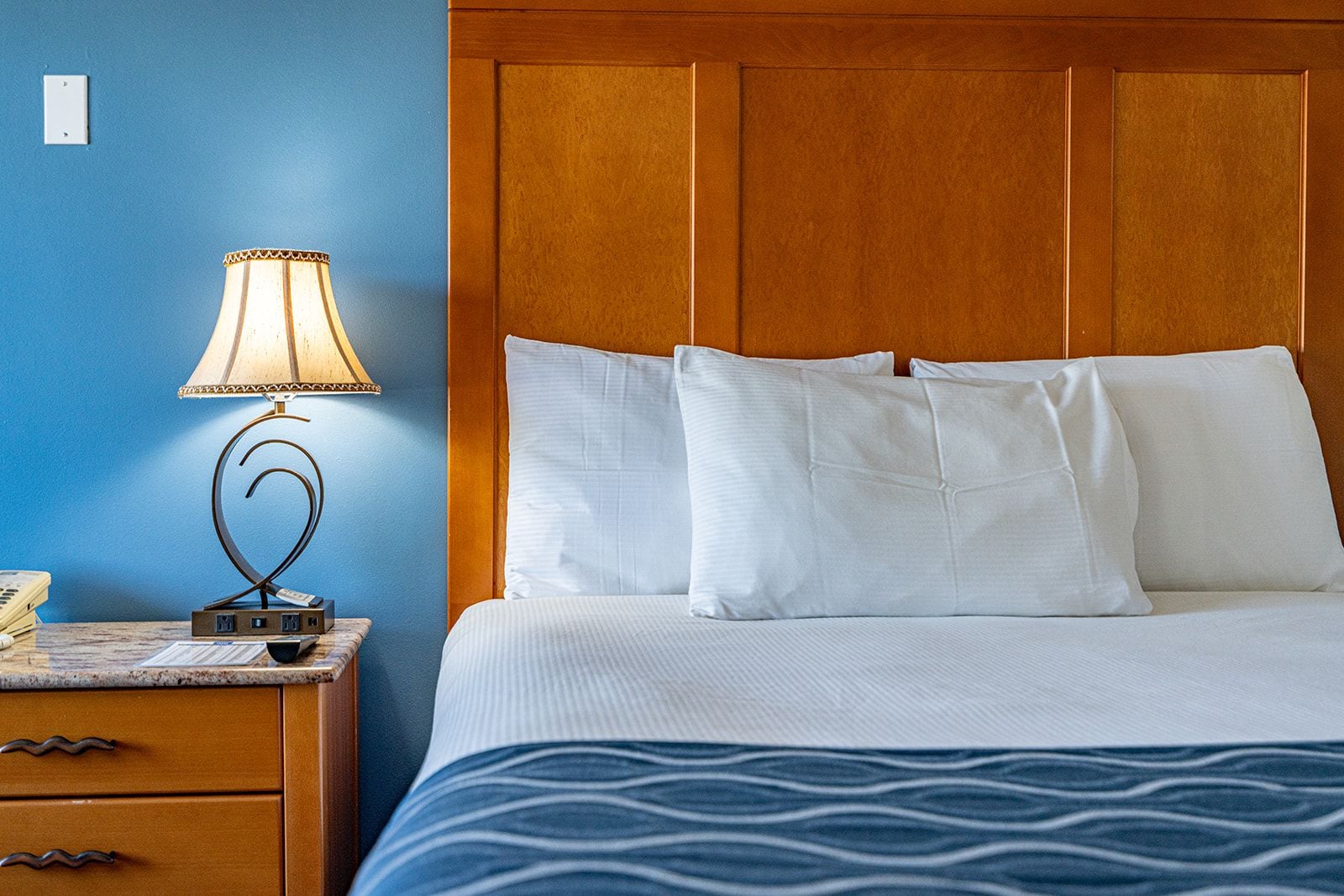 A hotel room with a bed, a nightstand with a lamp, and a telephone.