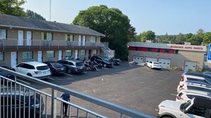 A parking lot with several cars and motorcycles, a building with a sign for 'MUSKOKA AUTO PARTS', and a large tree in the background. - Huntsville Inn (Huntsville)