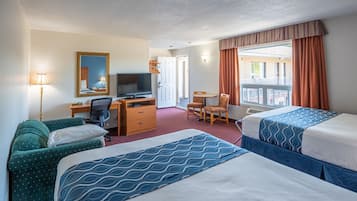 A hotel room with two beds, a desk with a television, a chair, and a window with curtains.