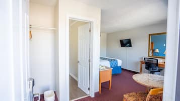 Ett hotellrum med en säng, ett skrivbord, en stol, en tv och en dörr som leder till ett annat rum.