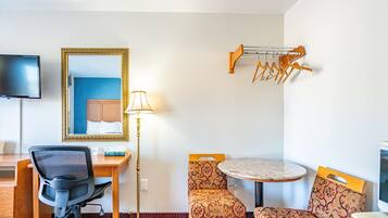 Une chambre d’hôtel équipée d’un bureau, d’une chaise, d’une table ronde, de chaises à motifs, d’une lampe, d’un miroir, d’une télévision et d’un porte-manteau.
