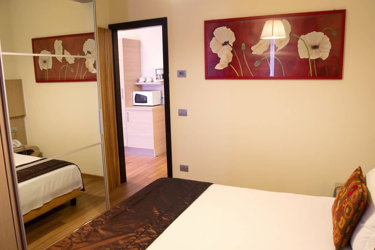 A hotel room with a bed, a wooden floor, a microwave, and two paintings of flowers on the wall.