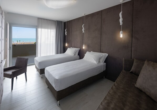 Habitación de hotel con dos camas, una silla y un balcón con vista a la playa.